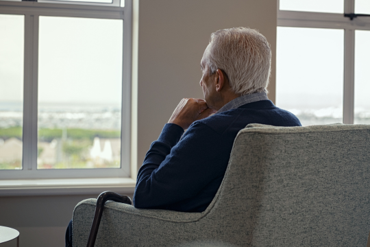 Man sitting in a chair pensively lokign out a window.