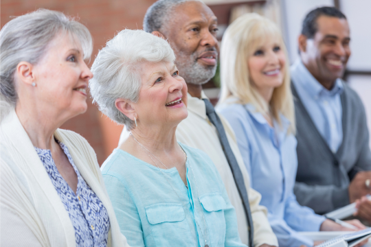 A group of older adults applaud at a town hall event.