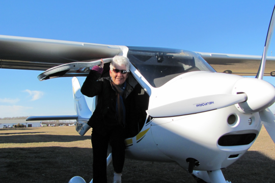 Barbara Biddle sitting in the doorway of a single-engine aircraft.