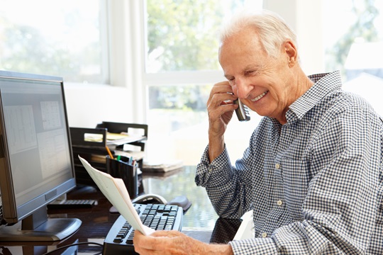 Un homme sur un téléphone en face de l'ordinateur de bureau.